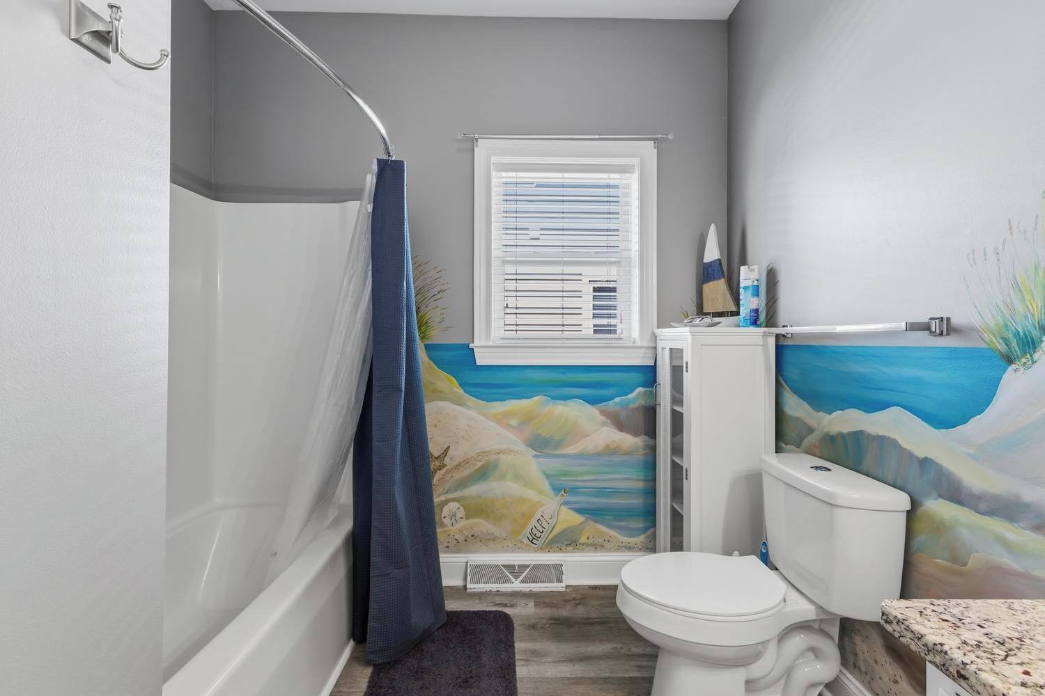 Ein Badezimmer mit Toilette, Dusche, einem Fenster mit Jalousien und einem Wandbild.