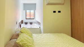 Een hotelkamer met een bed, een raam met uitzicht op gebouwen, een klein tafeltje met twee kopjes, en een houten deur.