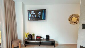A living room with a flat-screen TV mounted on the wall, a black entertainment unit with speakers and a small plant, and a decorative wall piece. - Baruch IV Itagüí: 2 bedrooms + private hot tub + balcony + A/C (Itagüí)