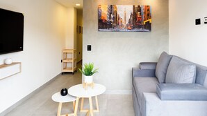 Uma sala de estar moderna com um sofá cinzento, uma mesinha redonda, uma planta em vaso e uma pintura de uma paisagem urbana.