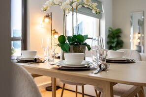 A dining table set with white bowls, plates, and cutlery, a vase with white flowers, and a potted plant. - Balcony Overlooking the Marina and Yachts, Near the Tram Station and Mall (Dubai)