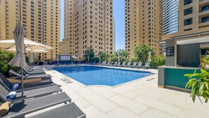 A swimming pool with lounge chairs and umbrellas, surrounded by tall residential buildings. - Balcony Overlooking the Marina and Yachts, Near the Tram Station and Mall (Dubai)