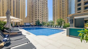 A swimming pool with lounge chairs and umbrellas, surrounded by tall residential buildings. - Balcony Overlooking the Marina and Yachts, Near the Tram Station and Mall (Dubai)