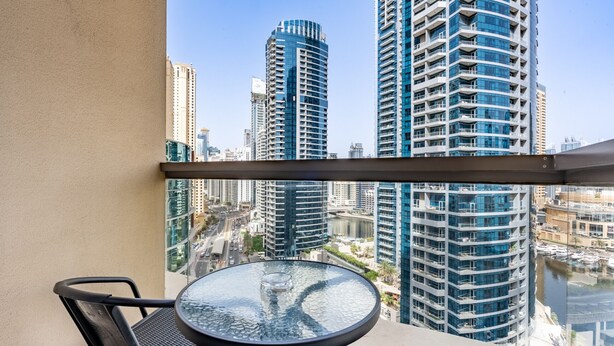 A balcony with a glass table and chairs, overlooking a cityscape with high-rise buildings and a marina. - Balcony Overlooking the Marina and Yachts, Near the Tram Station and Mall (Dubai)