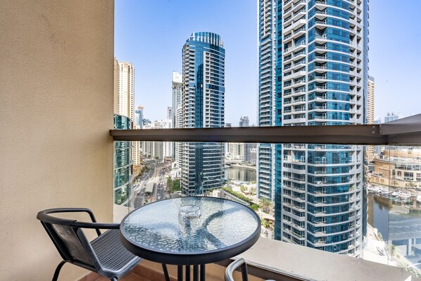 A balcony with a glass table and chairs, overlooking a cityscape with high-rise buildings and a marina. - Balcony Overlooking the Marina and Yachts, Near the Tram Station and Mall (Dubai)