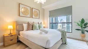 A modern bedroom with a bed, bedside table, lamp, artwork, window, and potted plant. - Balcony Overlooking the Marina and Yachts, Near the Tram Station and Mall (Dubai)