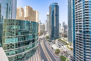 A modern urban skyline with high-rise buildings, a curved glass structure, and a multi-lane road. - Balcony Overlooking the Marina and Yachts, Near the Tram Station and Mall (Dubai)