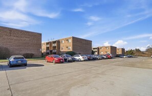 A parking lot with several cars and a brick building with multiple floors and balconies.