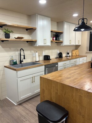 A kitchen with white cabinetry, wooden countertops, a black faucet, a toaster, a coffee maker, and a black trash bin.