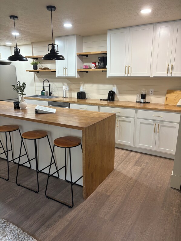 A modern kitchen with white cabinets, a wooden island, bar stools, and pendant lighting.