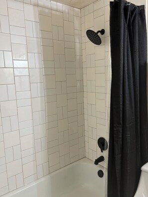 A bathroom with white tiled walls, a shower area, and a black shower curtain.
