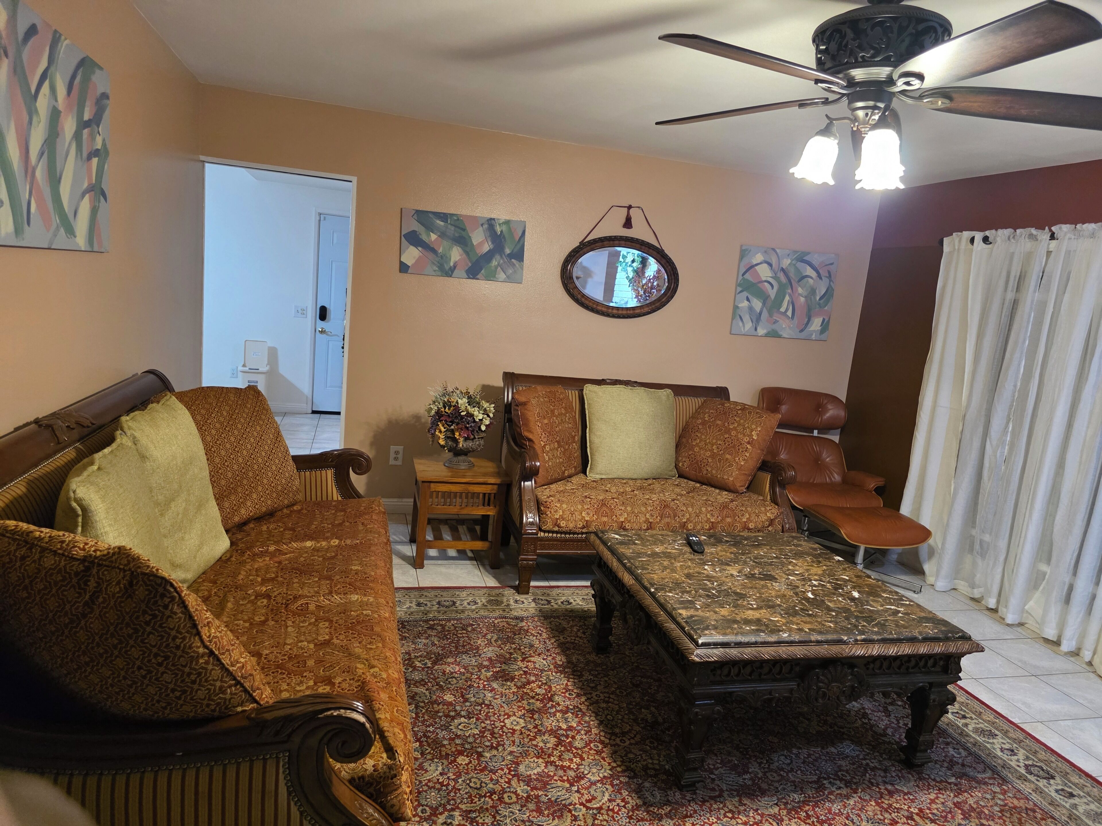 Uma sala de estar com sofá, poltrona, mesa de centro e ventilador de teto.