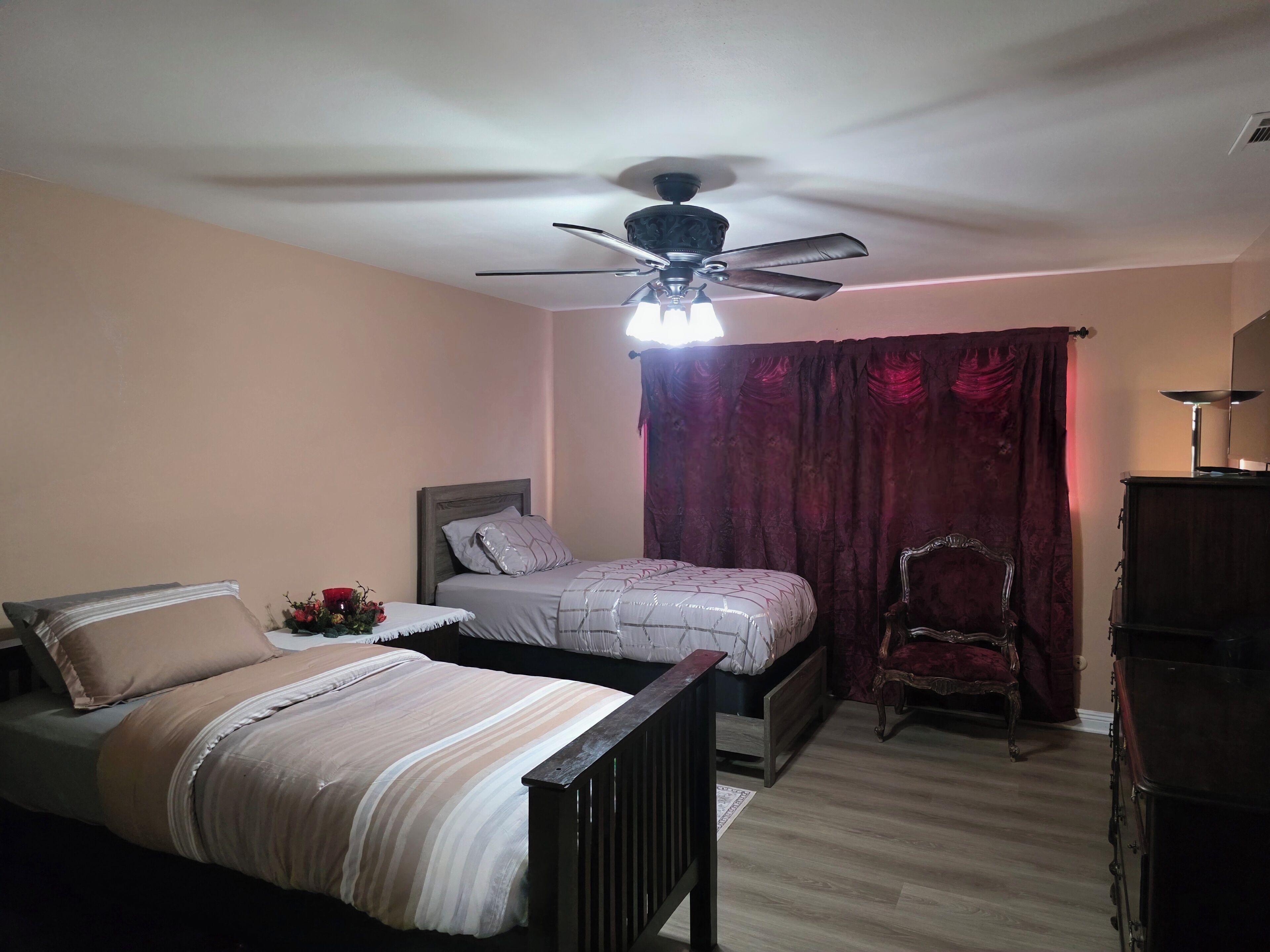 Un dormitorio con dos camas, un ventilador de techo, una silla y un aparador.