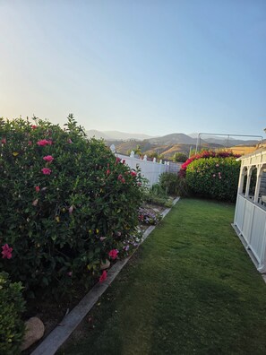 Un jardín cuidado con un seto blanco, un césped y vistas a colinas lejanas.