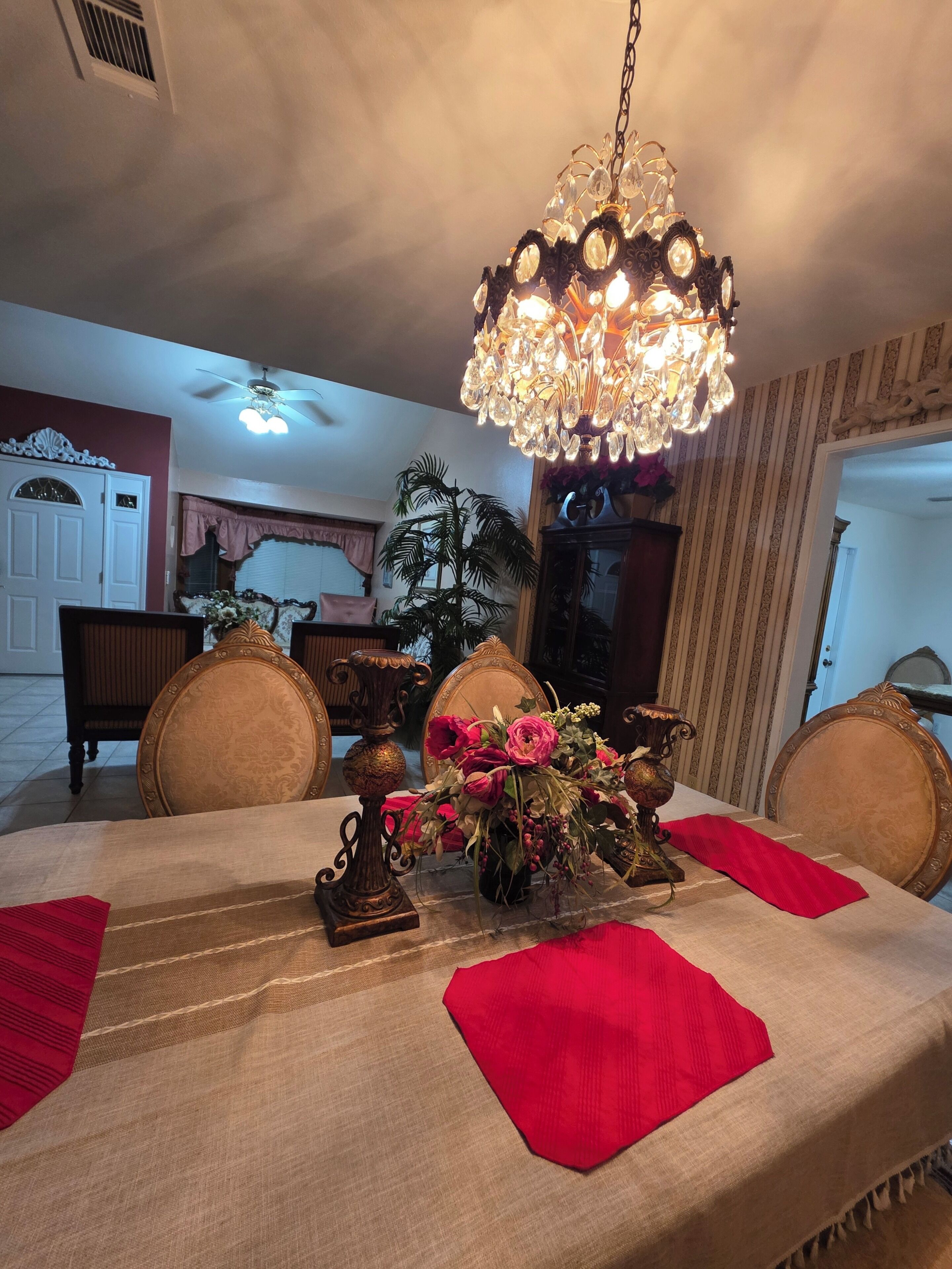 Un comedor con una araña, una mesa dispuesta con servilletas rojas y un jarrón de flores.