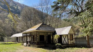 A traditional wooden house with a porch, surrounded by a fenced area and trees. - Landsitz Kammerburg - Landhaus mit Kegelbahn (Lorch)