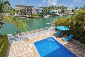 A pool area with a blue pool, lounge chairs, and a view of a marina with boats. - Spacious 4‑Bedroom Waterfront Retreat with Private Pool & 37.5' of Dockage. (Key Colony Beach)