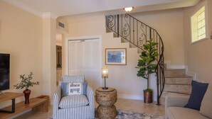Un salon avec un canapé à rayures, une table basse, un téléviseur et un escalier agrémenté d’une rampe décorative.