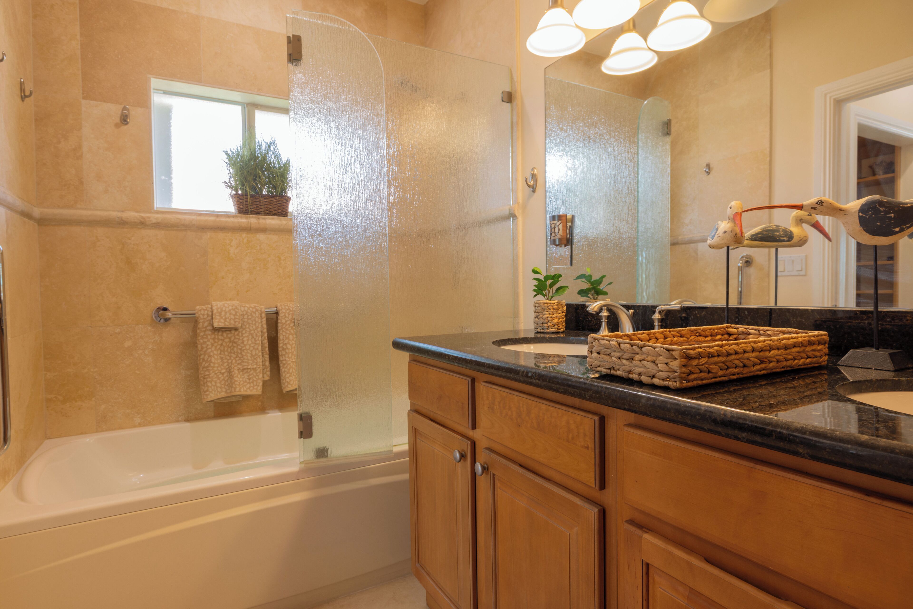 A bathroom with a bathtub, a sink, wooden cabinets, a mirror, and a window with a plant.