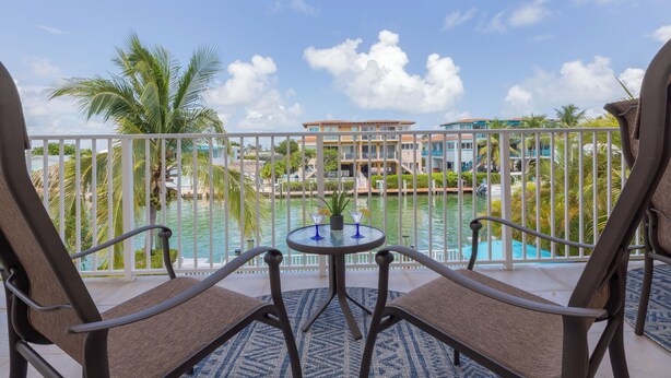 Un balcon avec vue sur une piscine, des palmiers et des bâtiments en arrière-plan.