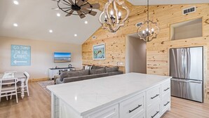 A modern kitchen with a large island, wooden wall paneling, and a stainless steel refrigerator.