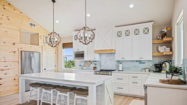 A modern kitchen with a large island, white cabinetry, and a wooden accent wall.