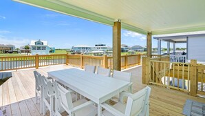 A covered outdoor deck with a white table and chairs, wooden railings, and a view of buildings across a body of water.