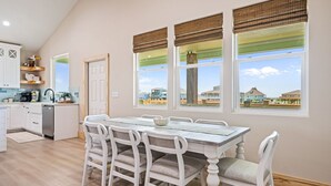 A dining area with a table and chairs, a kitchen with white cabinets, and large windows with views of buildings.
