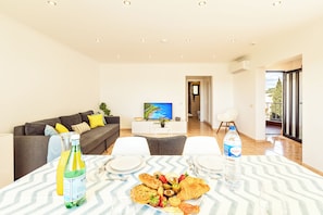 Ein modernes Wohnzimmer mit Essbereich, einer Couch, einem Fernseher und Blick auf einen Balkon.