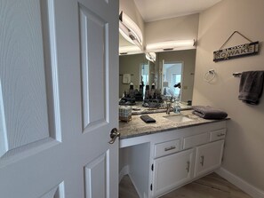 Une salle de bain avec un meuble-lavabo blanc, un évier, un miroir et un porte-serviettes.