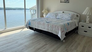 A bedroom with a large window, a bed with a patterned bedspread, a nightstand, and a wall decoration. - Escape to this top floor,  pet-friendly 3BR/3BA condo at Regatta Bay MM 12 (Lake Ozark)