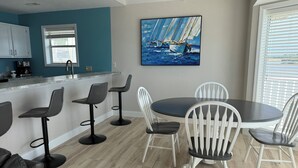 A modern kitchen with a bar area, a dining table with chairs, and a painting of sailboats on the wall. - Escape to this top floor,  pet-friendly 3BR/3BA condo at Regatta Bay MM 12 (Lake Ozark)