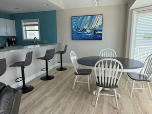 Een moderne keuken met een bar, een eettafel met stoelen en een schilderij van zeilboten aan de muur.