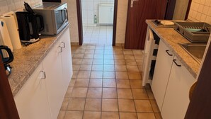 Una cocina estrecha con gabinetes blancos, microondas, hervidor y un lavabo.