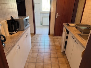 A narrow kitchen with white cabinets, a microwave, a kettle, and a sink.