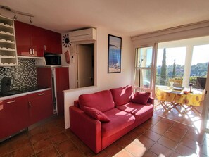 Ein kompakter Wohnbereich mit Küchenzeile, einem roten Sofa und einem Balkon mit Tisch und Stühlen.
