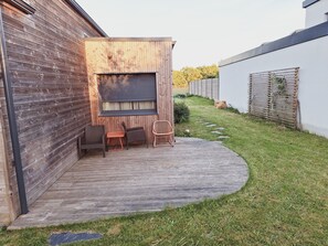 Eine Terrasse mit Holzdeck, einem Fenster mit Rollläden und drei Korbstühlen.