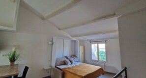 Une chambre à coucher avec un lit, une fenêtre, une table de chevet, une chaise et une plante.