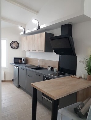 Une cuisine moderne avec des meubles gris, une hotte noire, un four à micro-ondes et un évier.