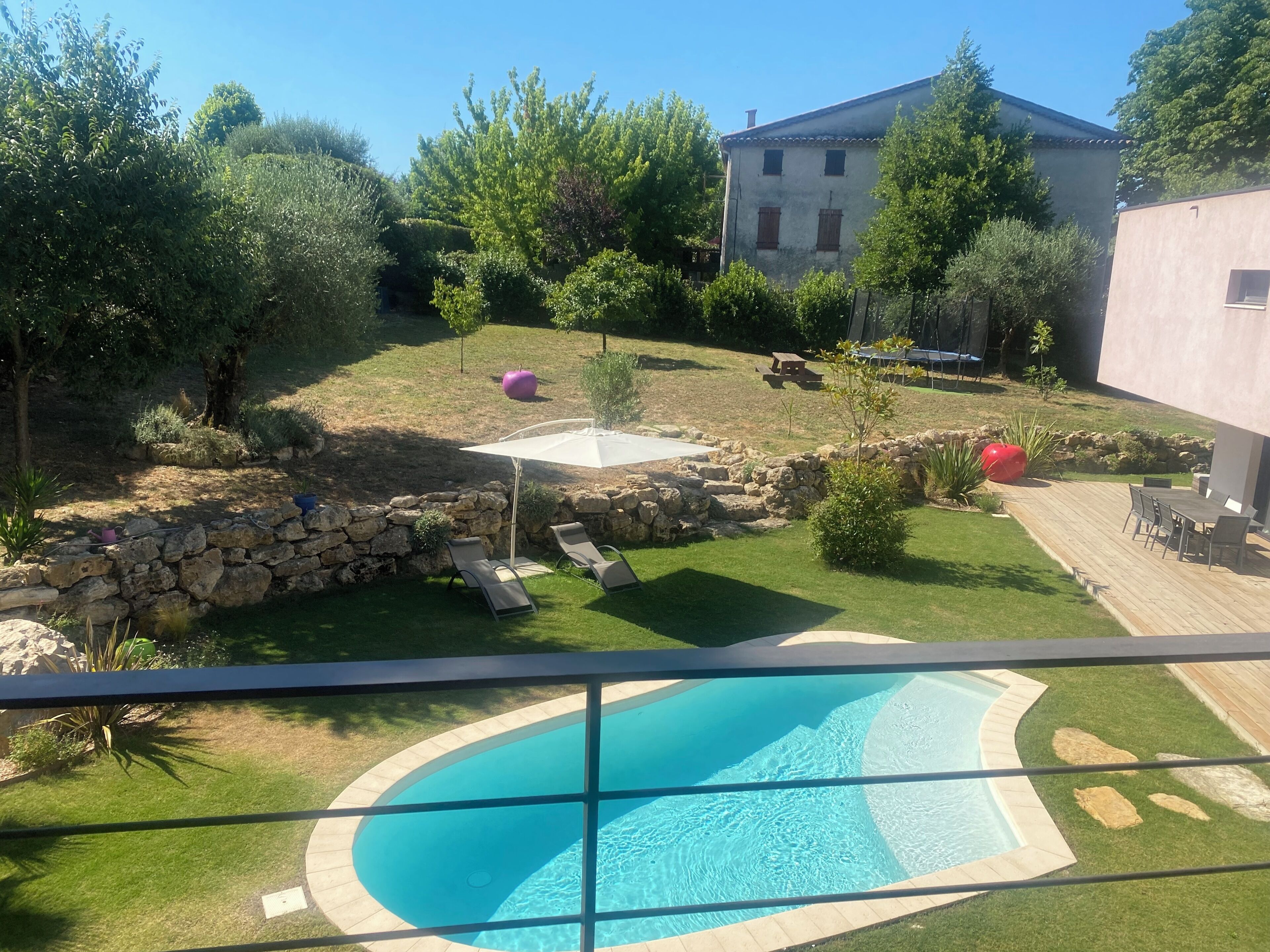 Uma piscina com borda de pedra, uma parede de pedra e uma área gramada com árvores e um edifício ao fundo.