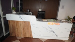 Ein Empfangsschalter mit Holz- und Marmordesign, ein schwarzer Bürostuhl und ein Blumentopf.