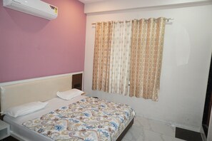 Un dormitorio con cama, cabecera, aire acondicionado instalado en la pared y ventana con cortinas estampadas.