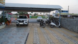 Ein überdachter Parkbereich mit befestigtem Weg, ein weißer SUV und mehrere Motorräder.