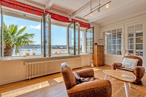 Une pièce dotée de grandes fenêtres, d’un radiateur, de fauteuils en cuir, d’une table en bois et d’un meuble.