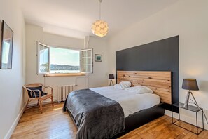 Une chambre avec un grand lit, une fenêtre donnant sur un paysage dégagé, une chaise, une table de chevet et une lampe.