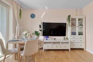 Ein Wohnzimmer mit Fernseher, Esstisch, Stühlen, einer Vitrine und einer Wanduhr.