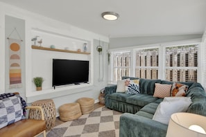 Ein Wohnzimmer mit Fernseher, einem grünen Sofa und einem karierten Teppich.