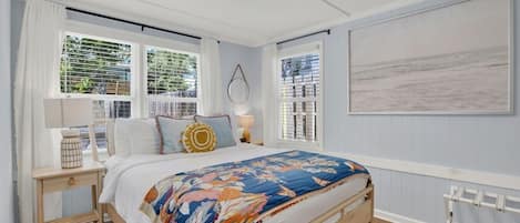A bedroom with a bed, two bedside tables, a window with blinds, a radiator, and a painting on the wall.