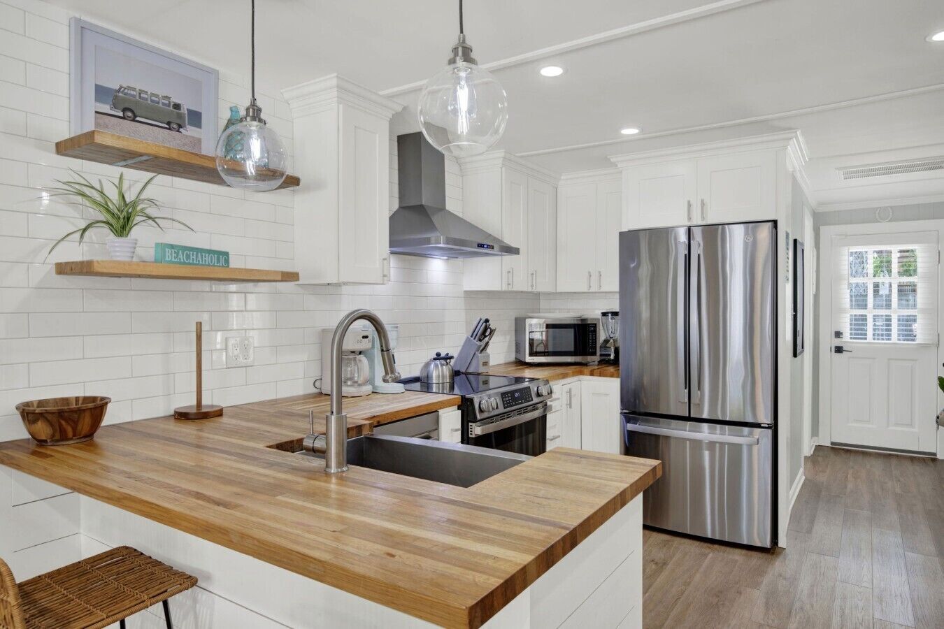 A modern kitchen with white cabinets, stainless steel appliances, a wooden countertop, and pendant lighting.