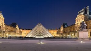 A large, illuminated building with a prominent pyramid-like structure in the center, surrounded by classical architecture. - Palais Royal - Prestige between the Louvre and the Opera (Paris)